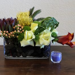 Mixed floral arrangement in a glass vase with a small blue candle beside it