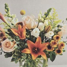 Bouquet of orange lilies, peach roses, and white blooms in a glass vase