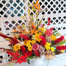 Large tropical bouquet with red, yellow, and orange flowers in a white vase