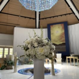 White floral arrangement on a tall pedestal in a ceremony space