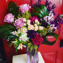 Mixed bouquet of pink, purple, and white flowers in a purple glass vase
