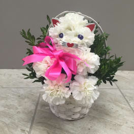 White floral cat face arrangement in a basket with a pink ribbon
