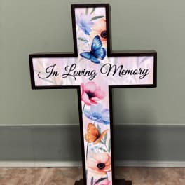 Cross-shaped memorial sign with floral and butterfly artwork and the words In Loving Memory