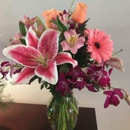 Mixed bouquet of pink lilies, roses, and a gerbera daisy in a glass vase