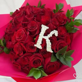 Bouquet of red roses wrapped in bright pink paper with a white floral letter