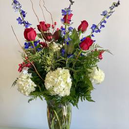 Tall bouquet of red roses, white hydrangeas, and blue flowers in a glass vase