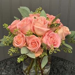 Pink roses arranged in a clear glass vase with greenery