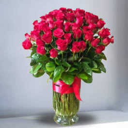 Tall arrangement of red roses in a clear glass vase with a red ribbon