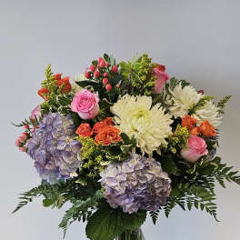 Mixed bouquet of roses, hydrangeas, and white chrysanthemums in a glass vase