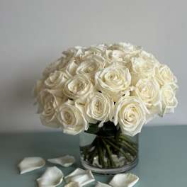 Bouquet of white roses in a clear glass vase with scattered petals