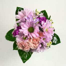 Compact bouquet of pink daisies, peach carnations, and purple blooms in a rounded cluster