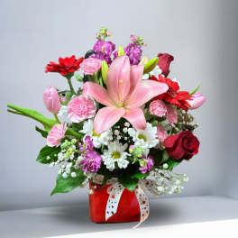 Mixed bouquet with a pink lily, red gerbera daisies, and roses in a red vase