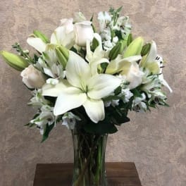 White lilies and roses arranged in a clear glass vase