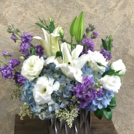 White lilies and blue hydrangeas with purple flowers in a dark vase