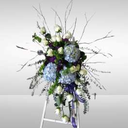 Tall floral spray with white roses, blue hydrangeas, and purple accents on an easel