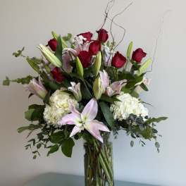 Tall bouquet of red roses, pink lilies, and white hydrangeas in a glass vase