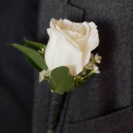 White rose boutonniere pinned to a dark suit jacket