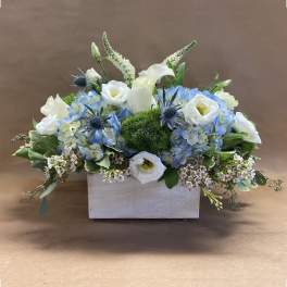 Blue and white floral arrangement in a white rectangular container