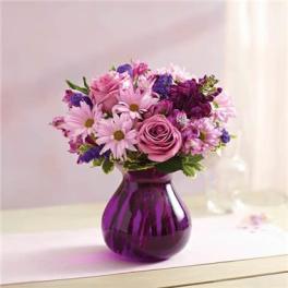 Pink roses and daisies with purple flowers arranged in a round purple glass vase