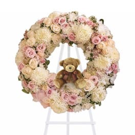 Pastel floral wreath with a teddy bear in the center on a white stand