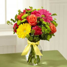 Colorful bouquet of mixed flowers in a clear glass vase with a yellow ribbon