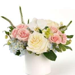Low arrangement of pastel roses, hydrangeas, and an orchid in a white cylinder vase