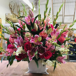 Large pink and red floral arrangement in a white container
