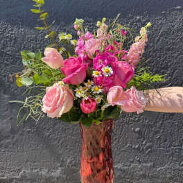Tall pink glass vase with mixed bouquet of pink roses, tulips, stock, and small white daisies.