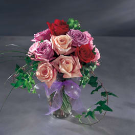 Bouquet of red, pink, and peach roses in a glass vase with a purple ribbon