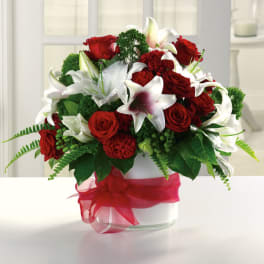 Red roses and white lilies arranged in a glass vase with a red ribbon