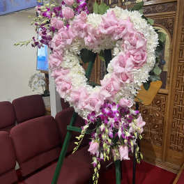 Heart-shaped floral wreath with pink roses and white flowers on an easel