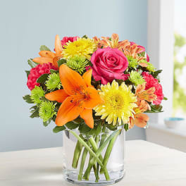 Bouquet of orange lilies, pink roses, and yellow daisies in a clear glass vase