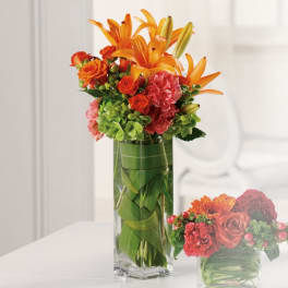 Orange lilies and roses arranged in a tall glass vase