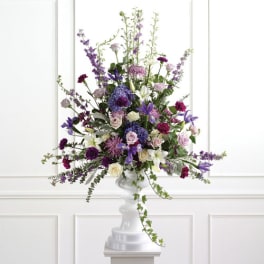 Tall purple and white floral arrangement in a white pedestal vase
