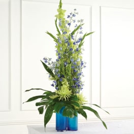 Tall blue and green floral arrangement in two blue glass vases