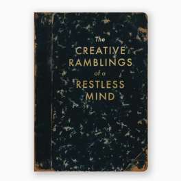A worn black book cover with gold text reading "The Creative Ramblings of a Restless Mind".