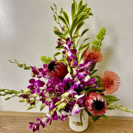 Tropical floral arrangement with purple orchids and red protea in a white vase