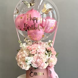 Pink birthday balloon above a pastel flower arrangement in a pink box