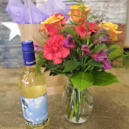 Bouquet of mixed flowers in a glass vase beside a small wine bottle