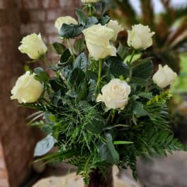 White roses arranged in a tall vase with dense greenery
