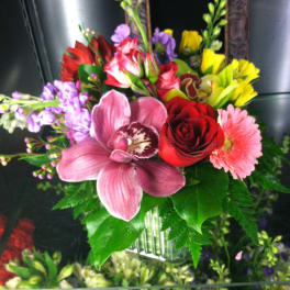 Mixed bouquet with pink orchid, red rose, pink gerbera and yellow blooms in a clear glass vase
