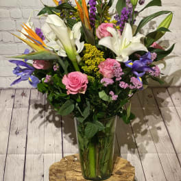 Tall mixed bouquet with white lilies, pink roses, and purple flowers in a glass vase