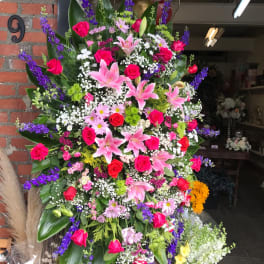 Large standing floral spray with pink lilies, red roses, and purple flowers