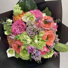 Mixed bouquet of pink, coral, and green flowers wrapped in black paper