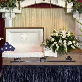Sympathy casket spray with white lilies and roses beside an open casket
