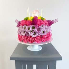Pink and lavender flower cake with candles on a white pedestal stand