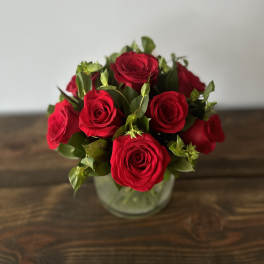 Compact arrangement of red roses in a clear glass vase on a wooden surface