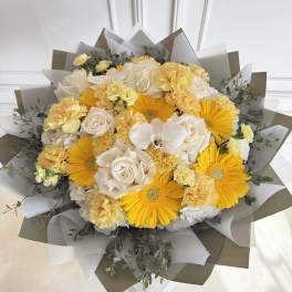 Bouquet of yellow gerbera daisies, white roses, and pale carnations wrapped in paper