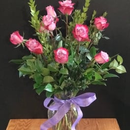 Pink roses in a clear glass vase tied with a purple ribbon
