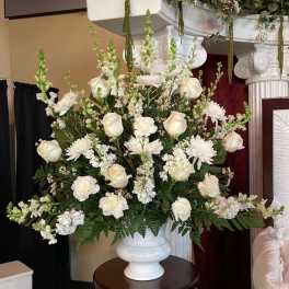 Large white arrangement of roses, carnations, and chrysanthemums in a white urn-style vase